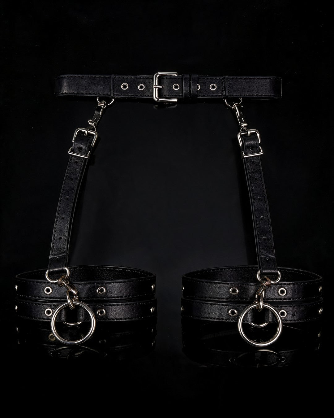 Dominatrix black faux-leather harness belt with thigh cuffs and silver O-rings, black background